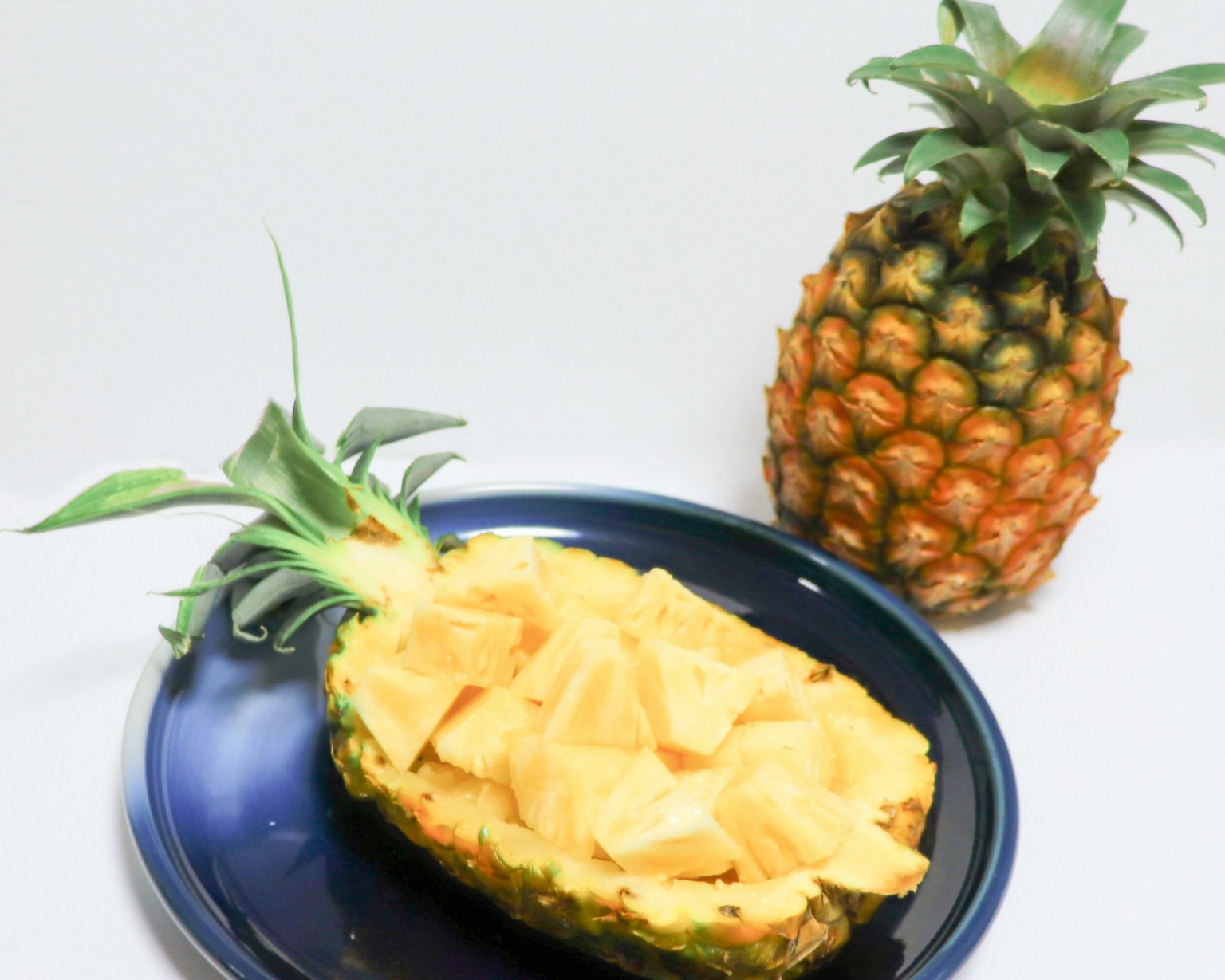 Un ananas coupé rempli de morceaux de fruits sur une assiette bleue à côté d'un ananas entier