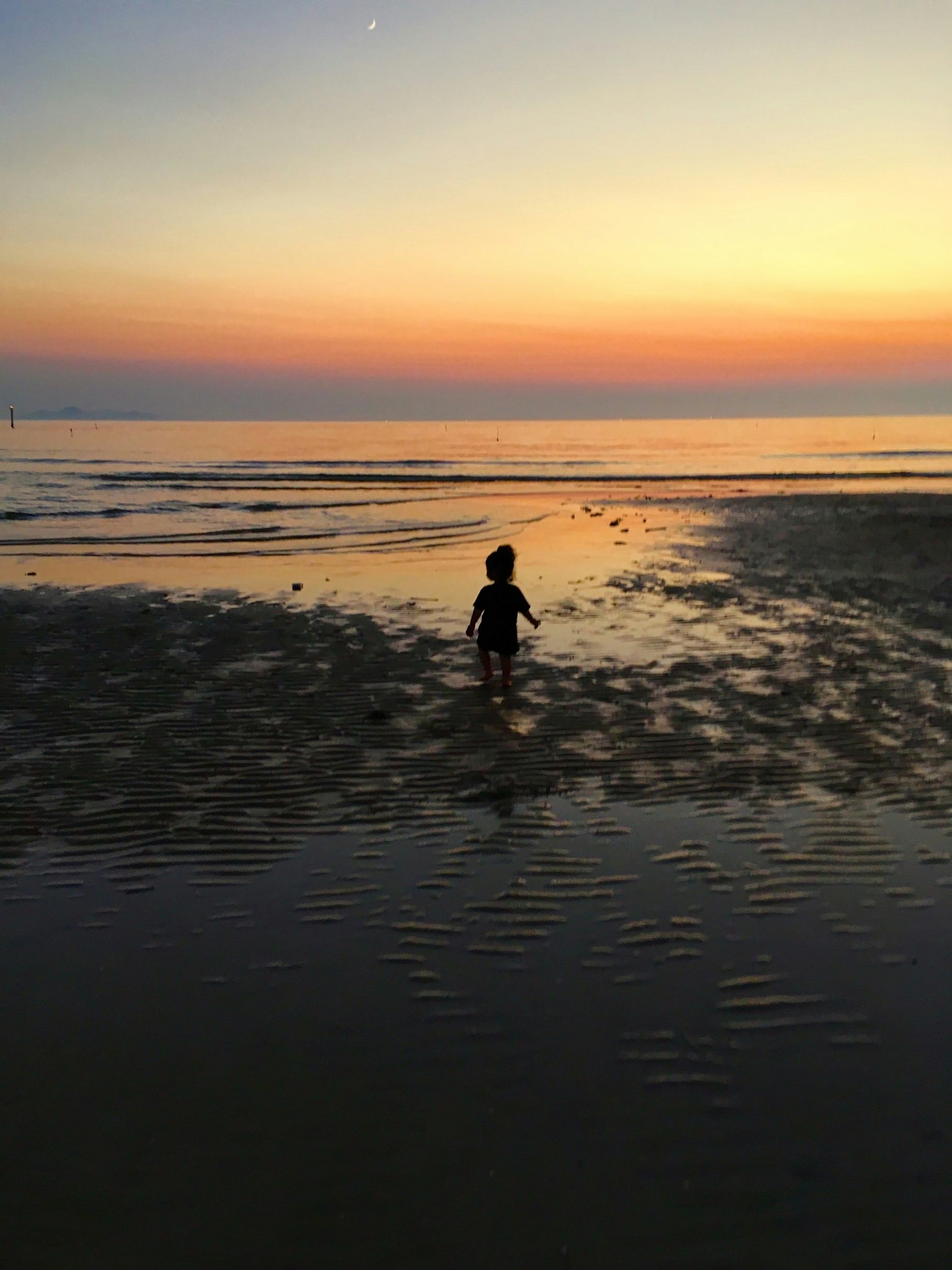 Silhouette eines Kindes, das bei Sonnenuntergang im Ozean spielt