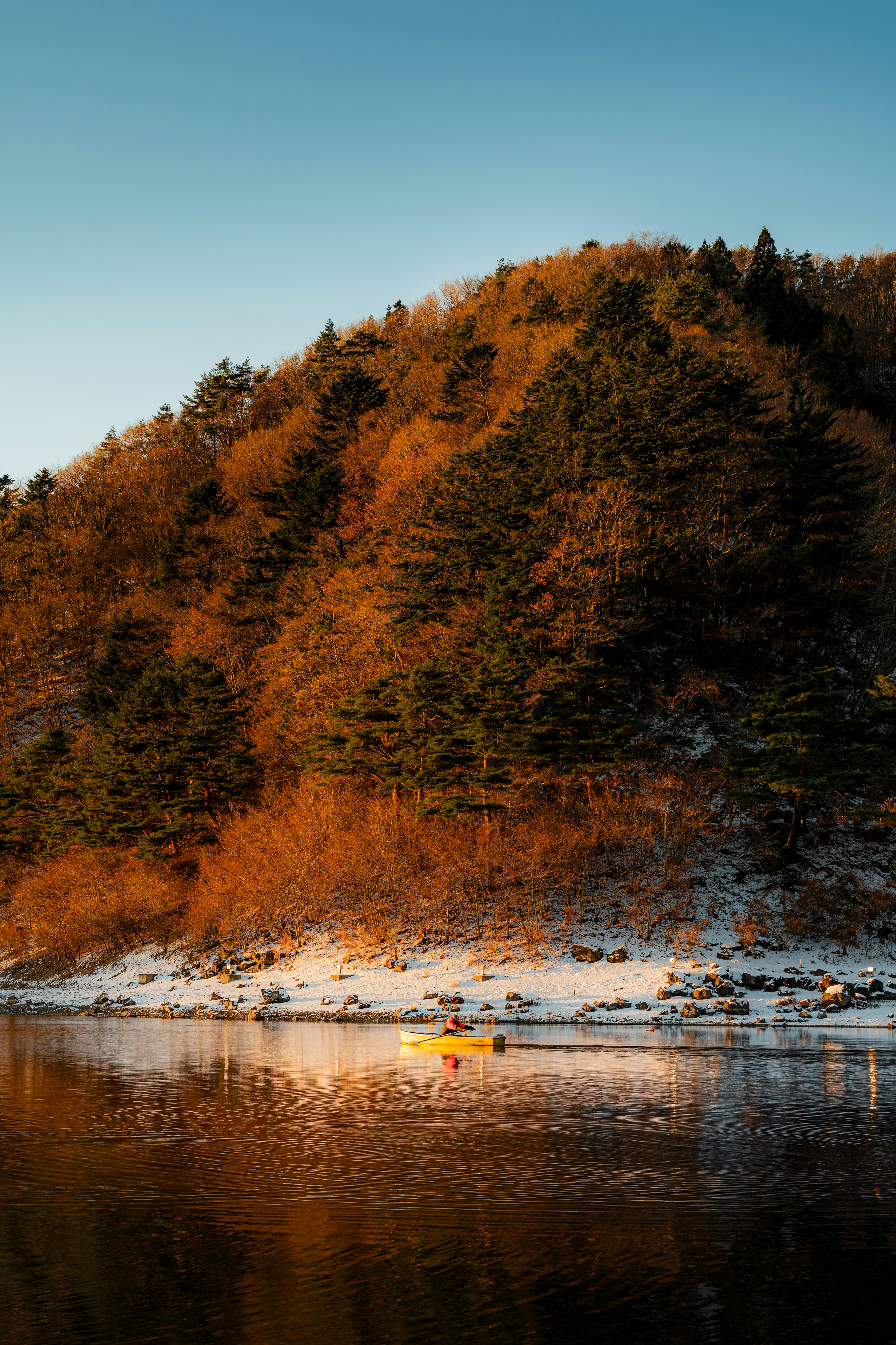 Une berge de rivière sereine avec des collines enneigées se reflétant dans des eaux calmes