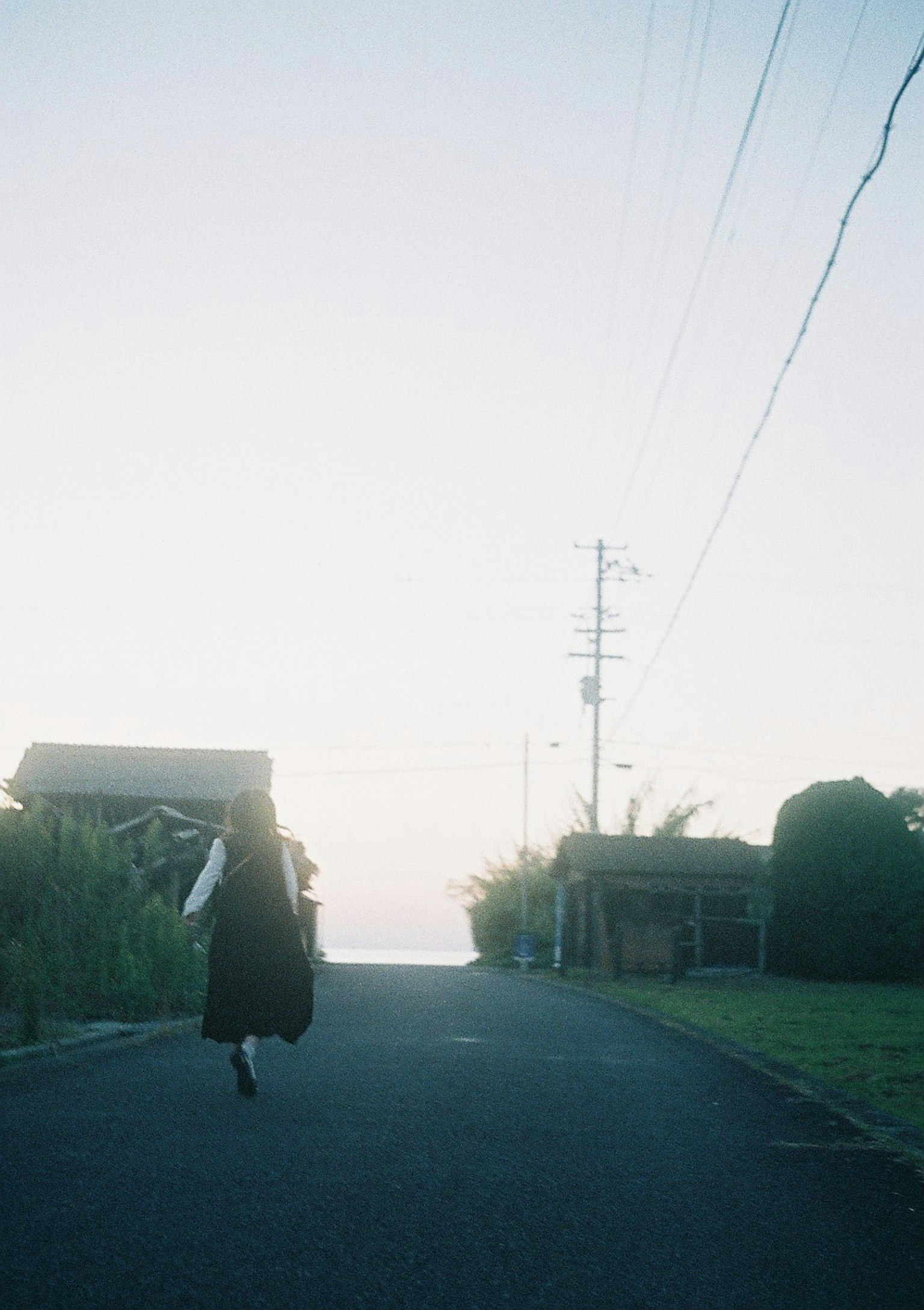 Silhouette of a person in black walking down a quiet road at dusk