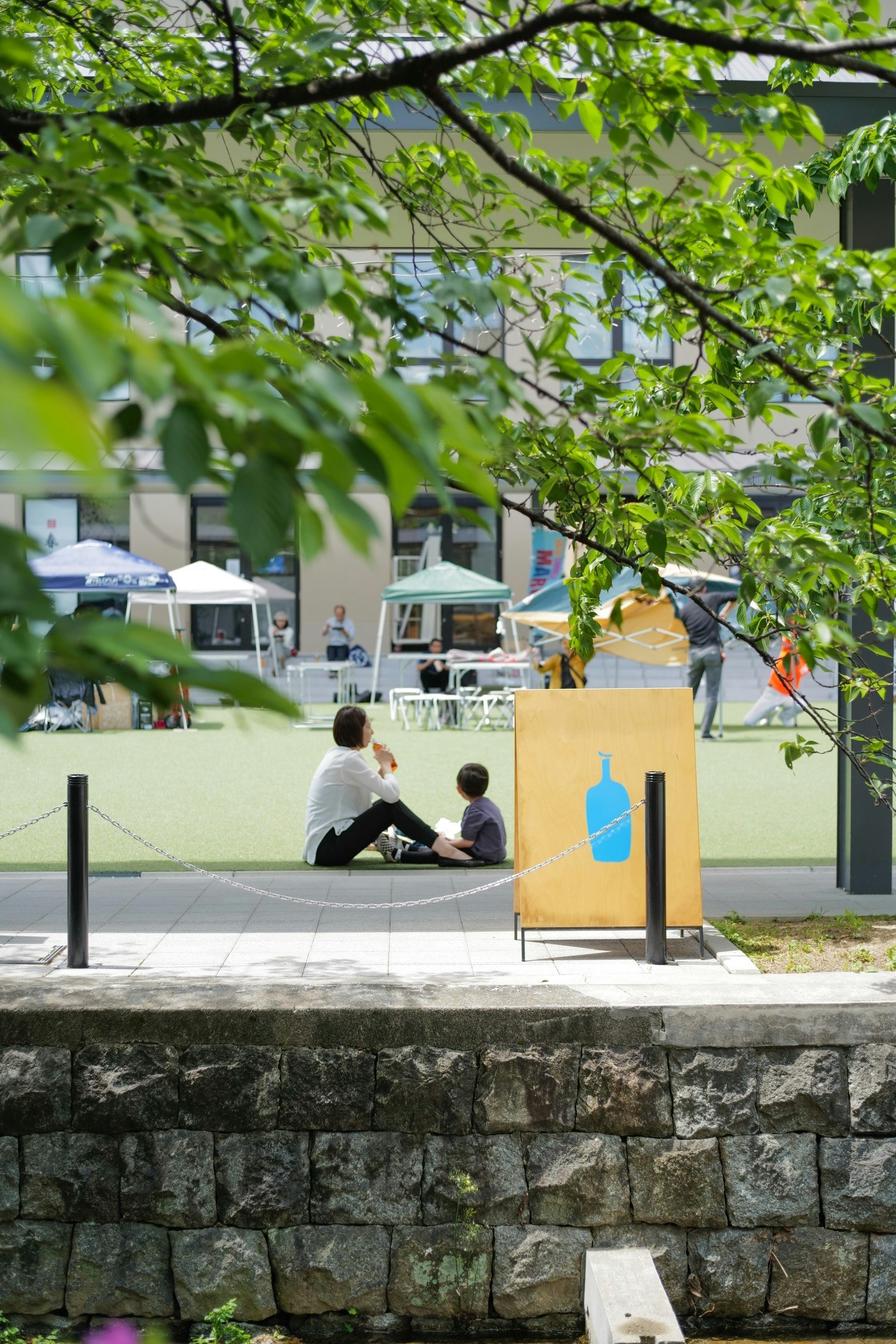 Un parent et un enfant assis sur l'herbe dans un parc avec un panneau de bouteille bleue