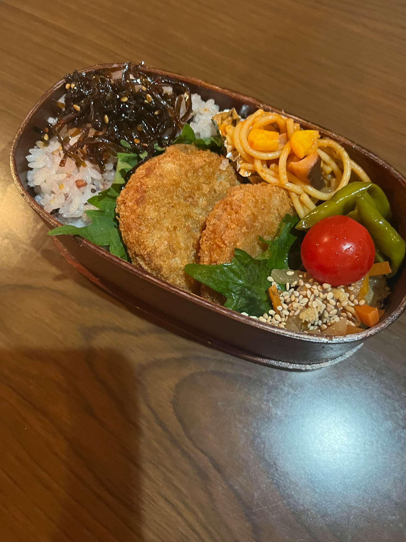 Eine Bento-Box mit Reis, Kroketten, Gemüse, Kirschtomaten und Spaghetti