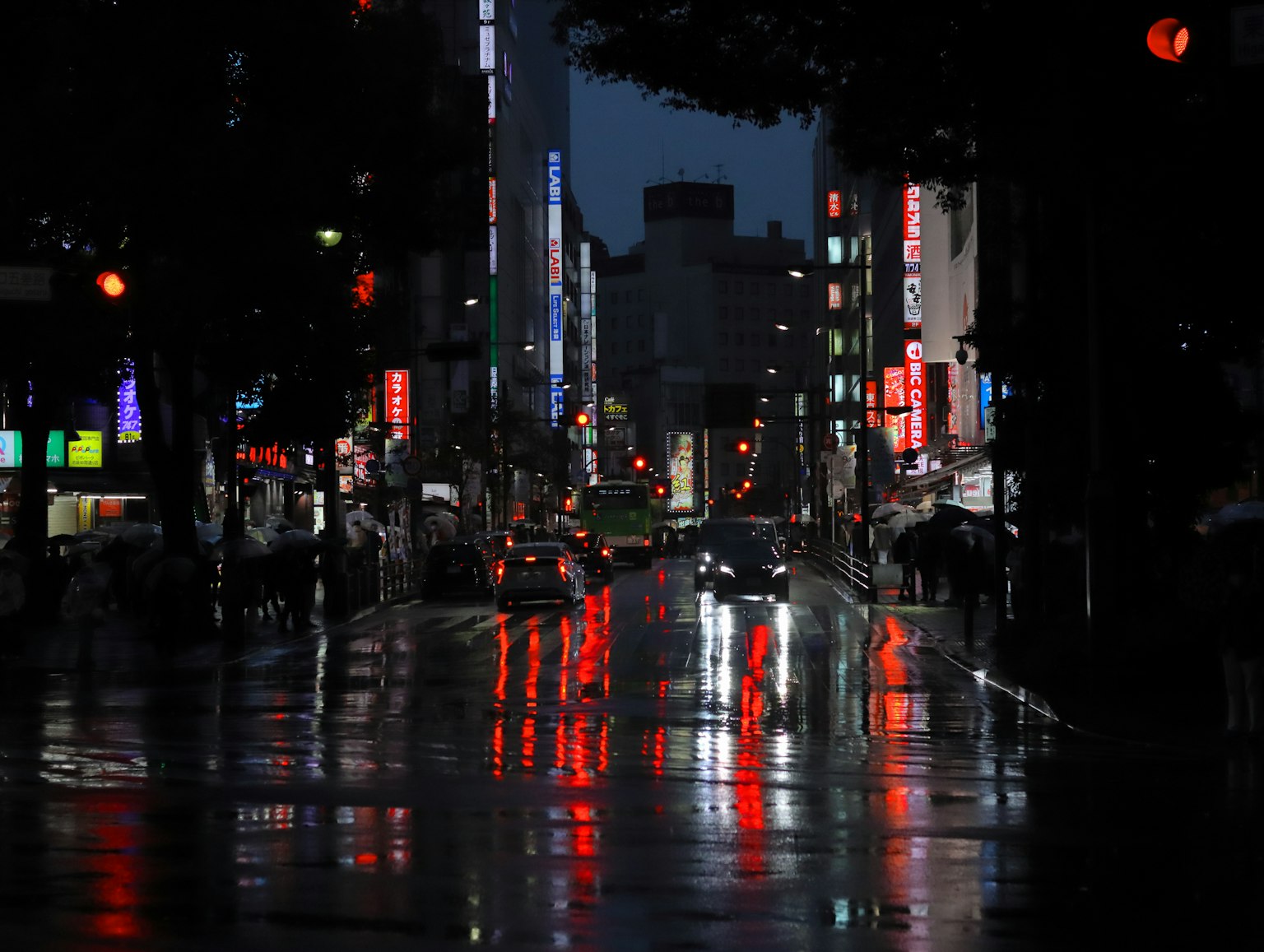ภาพเมืองในเวลากลางคืนพร้อมการสะท้อนของแสงสีแดงและถนนเปียก