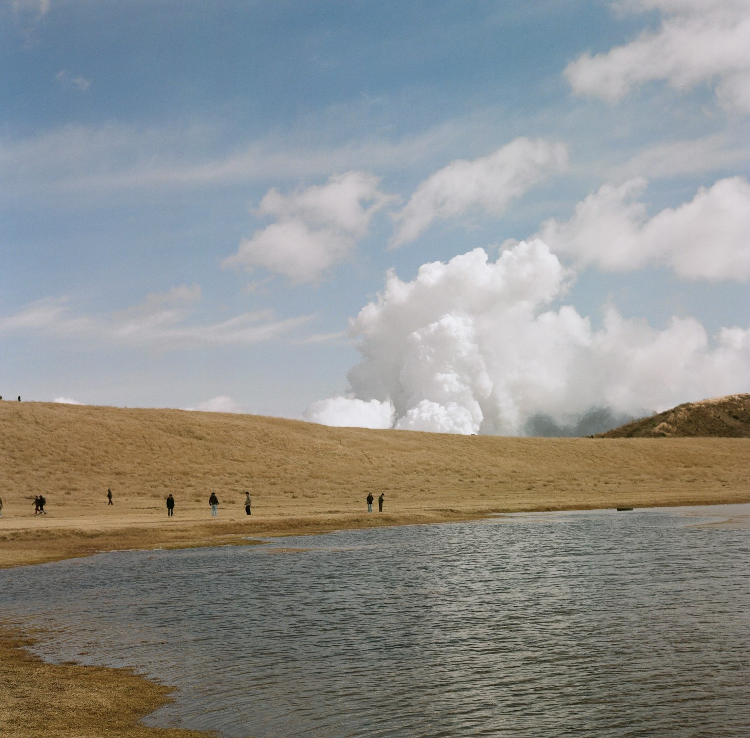 Landschaft mit einem ruhigen See und einem Sandstrand unter einem blauen Himmel und flauschigen Wolken