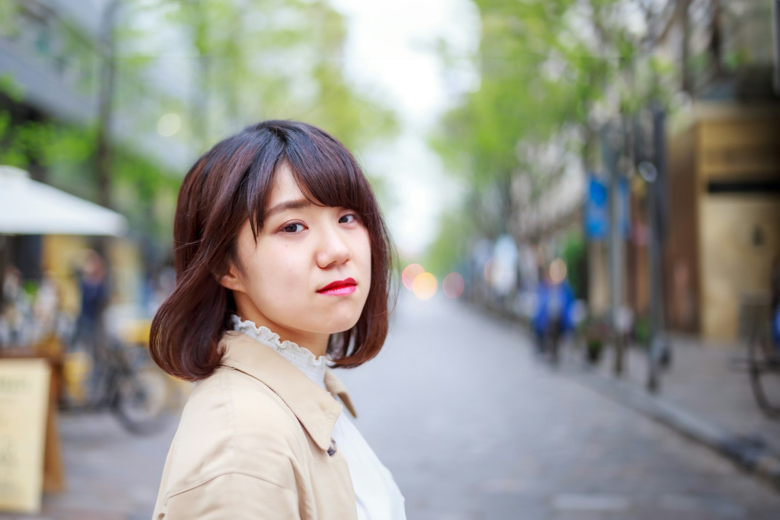 A woman looking back on a street lined with green trees