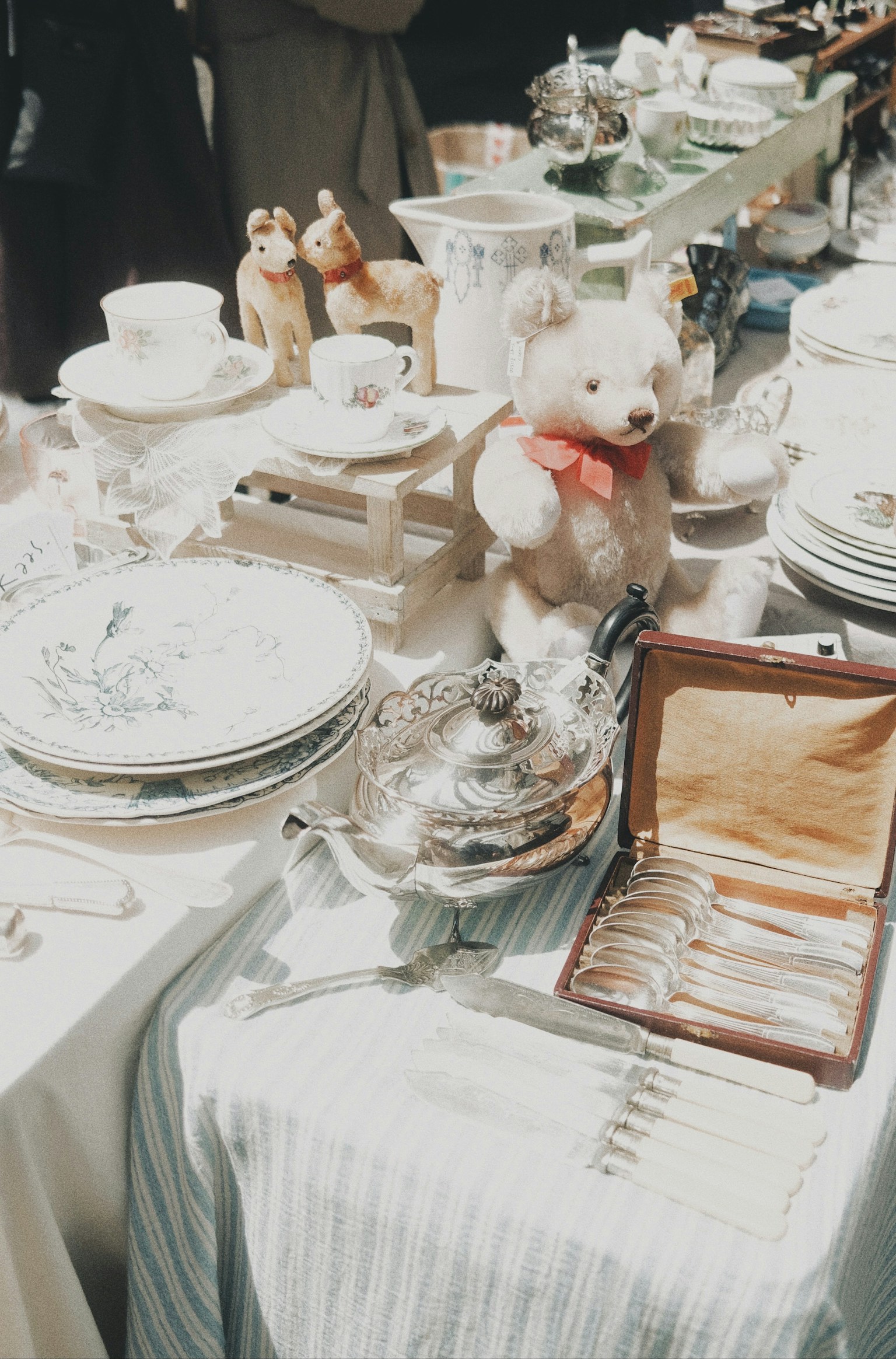 A table set with various dishware and silverware featuring a teddy bear with a red ribbon