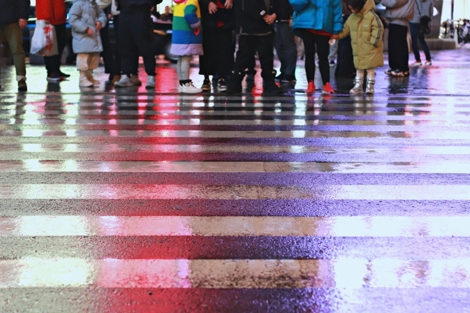 Close-up of people's feet standing on a wet crosswalk