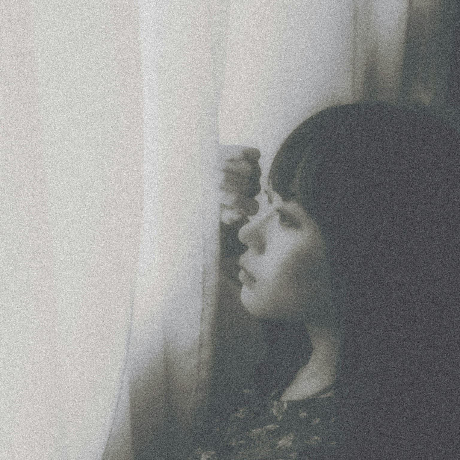 Black and white photo of a woman gazing out through a curtain