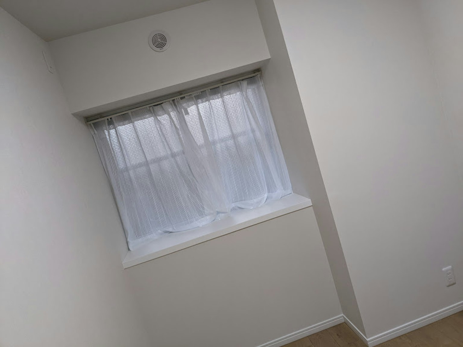 Habitación con paredes blancas y una ventana con cortinas transparentes