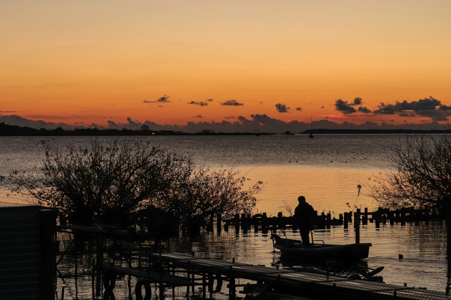 Una persona en una pequeña barca en un lago tranquilo al atardecer con siluetas de árboles