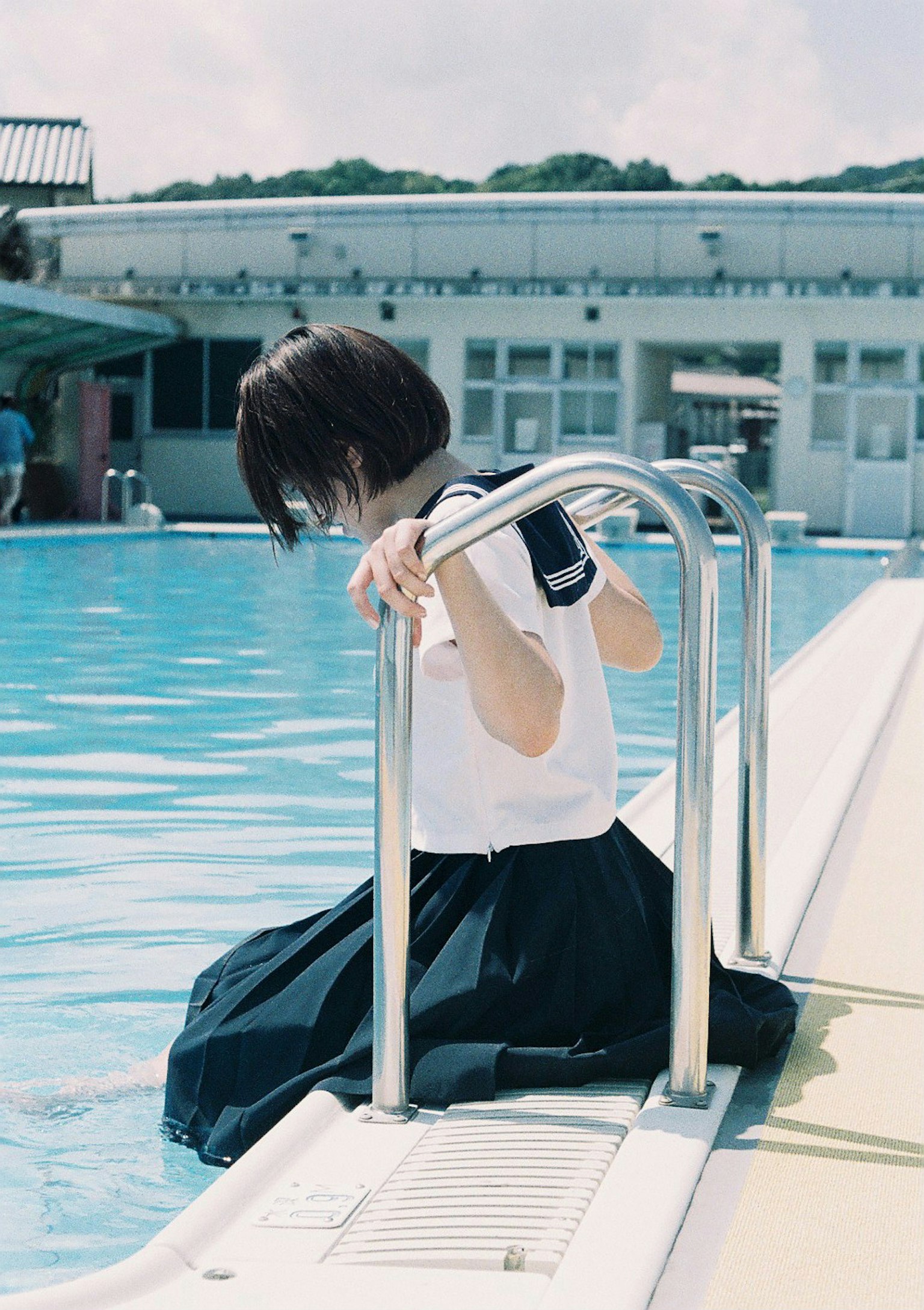 Girl in a school uniform dipping feet in a swimming pool