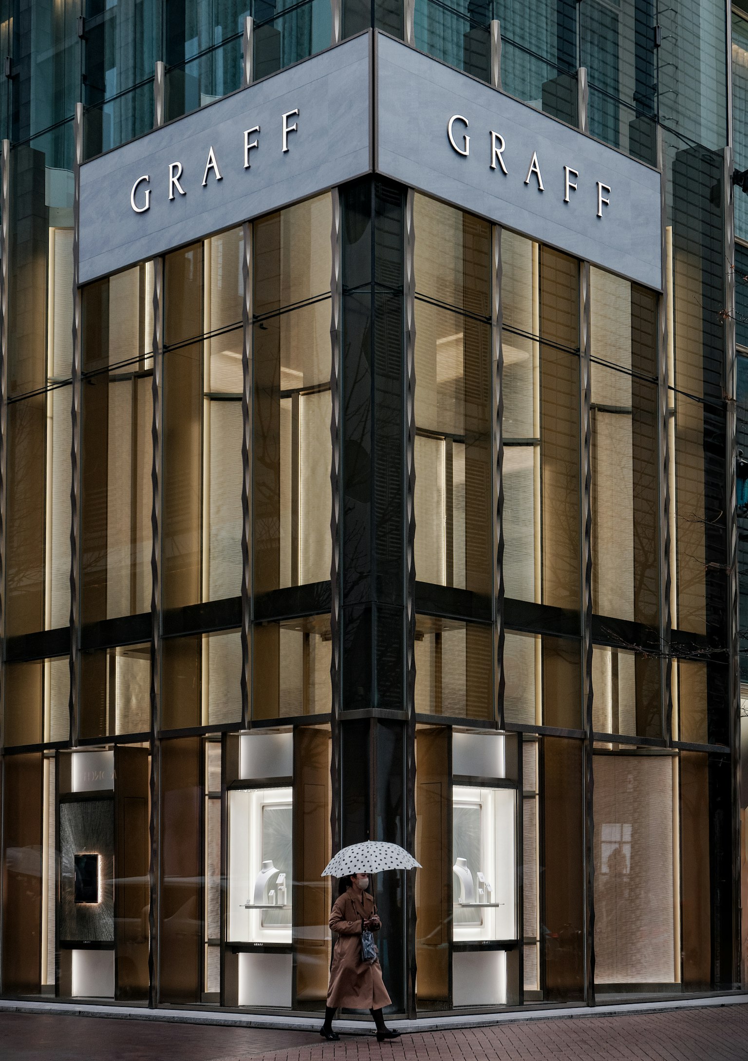 Exterior of luxury jewelry store Graff glass building person with umbrella in the rain