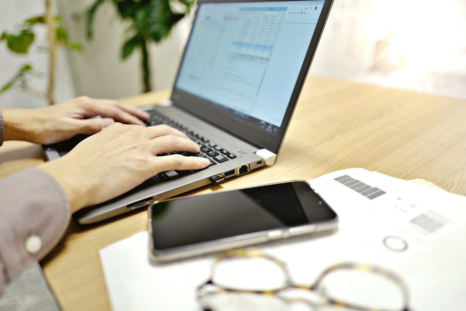 Mains tapant sur un ordinateur portable avec un smartphone et des documents sur un bureau
