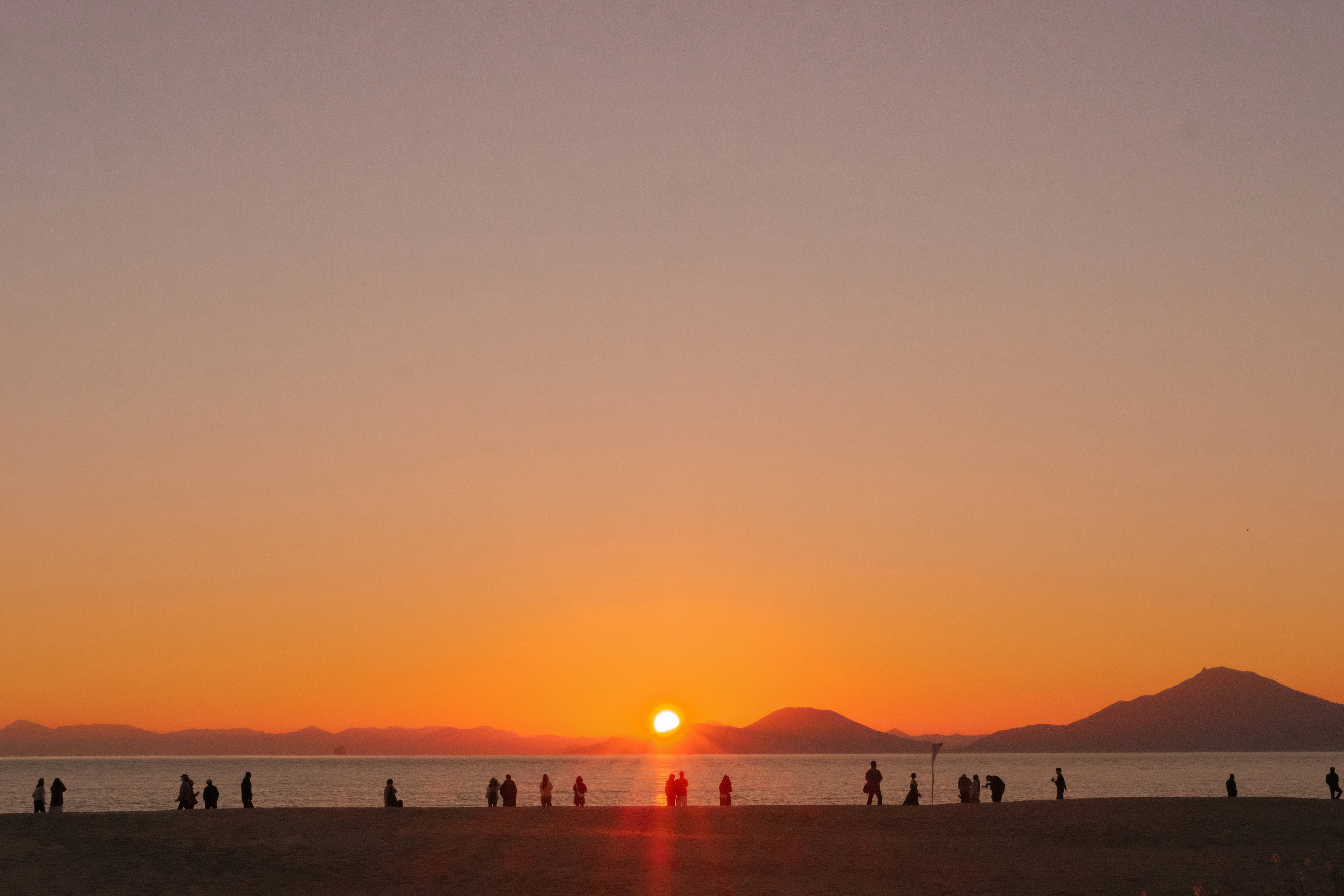 夕日に照らされる海辺の人々と水平線