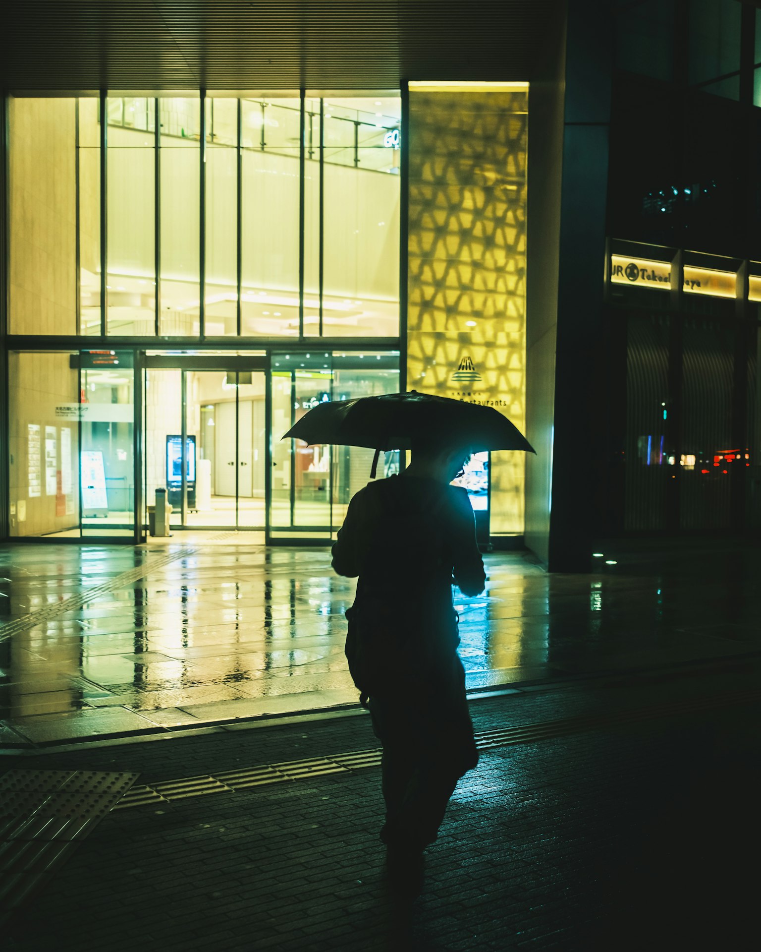 一個人在雨中拿著傘走在現代建築前