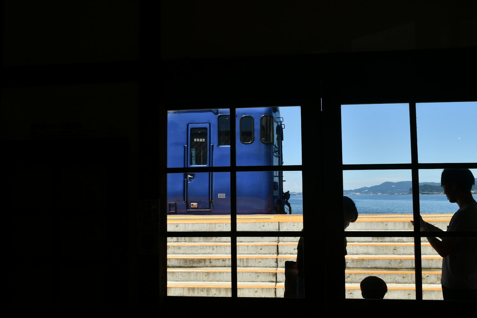 Silhouette di persone con un treno blu visibile attraverso una finestra
