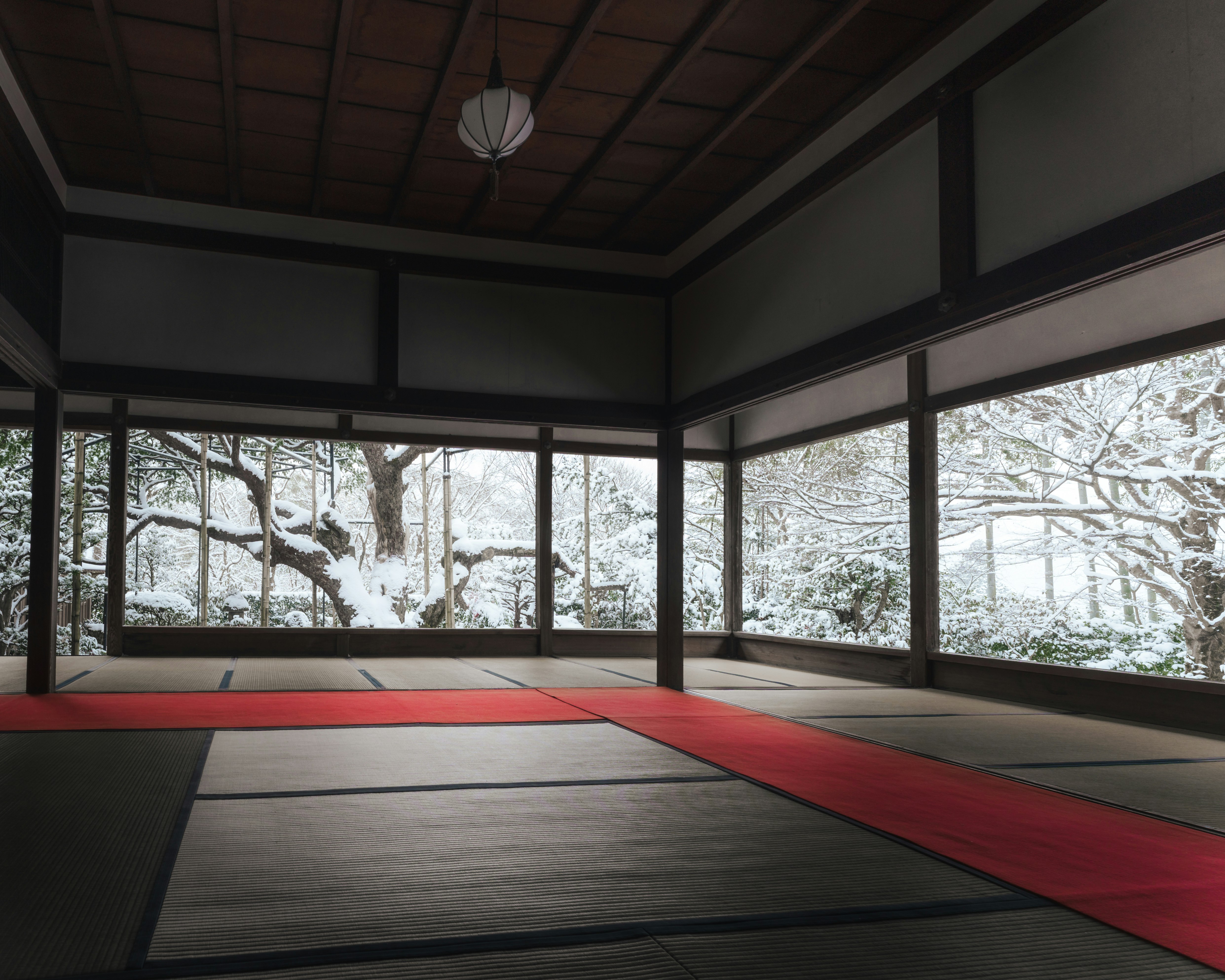 雪景色を望む和室の畳と赤い座布団のある空間