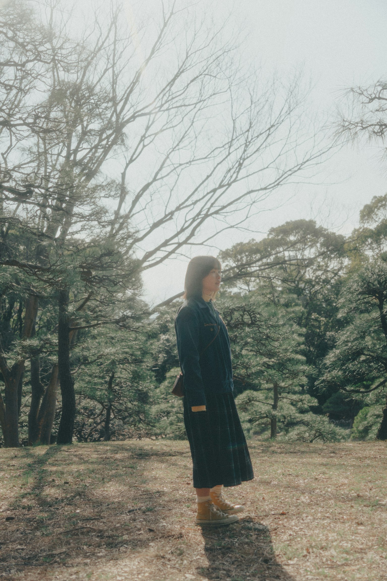 Side profile of a woman standing in nature with trees in the background