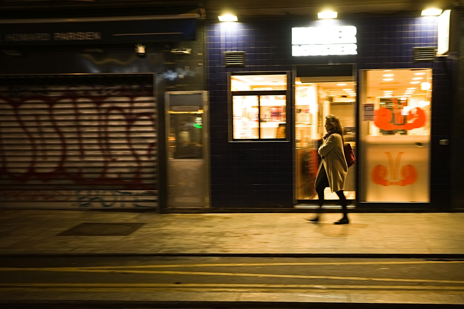 Donna che cammina in una strada notturna con finestre di negozi illuminate