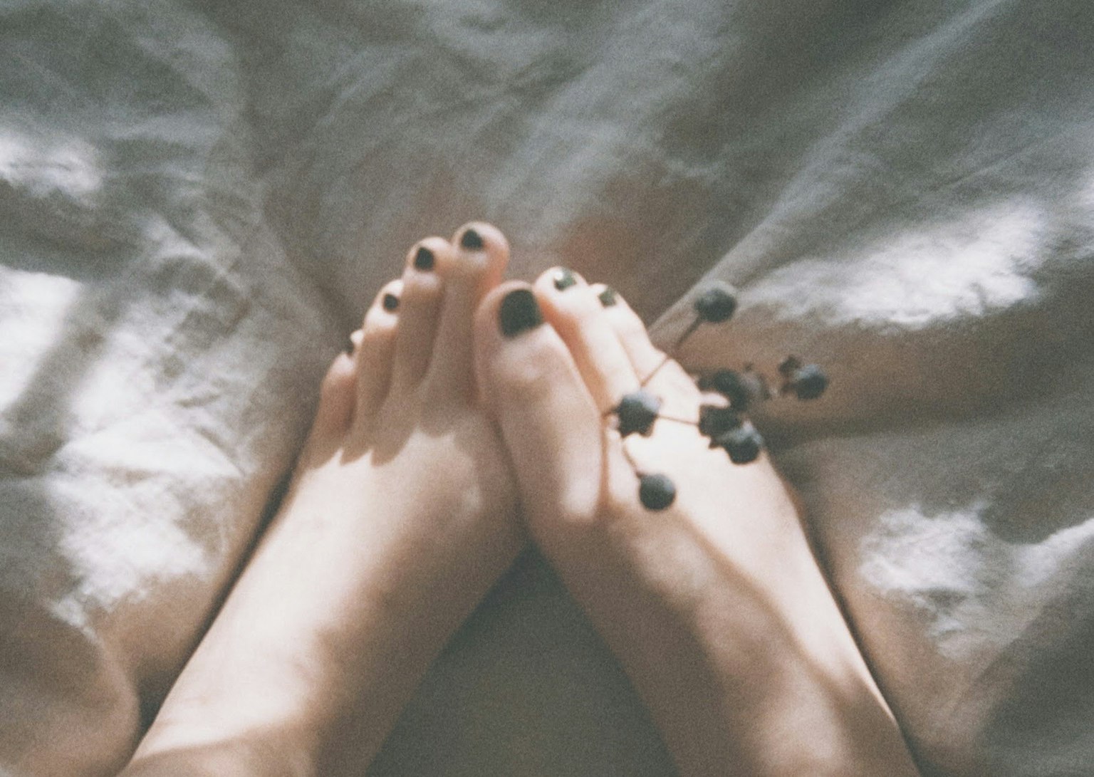 Foto di piedi con smalto scuro e piccole bacche posizionate tra di essi su un tessuto morbido