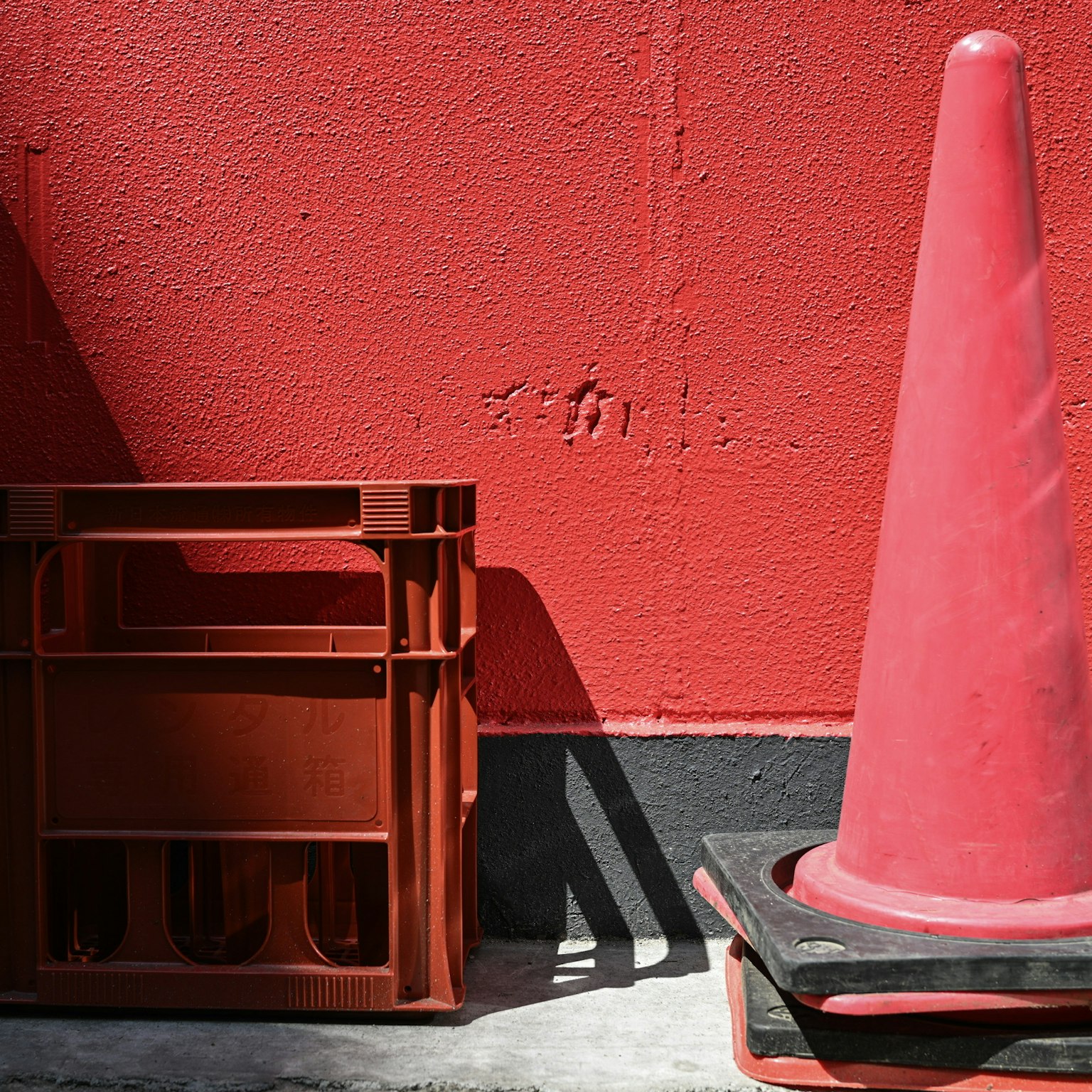 Red traffic cone and plastic crate against a red wall