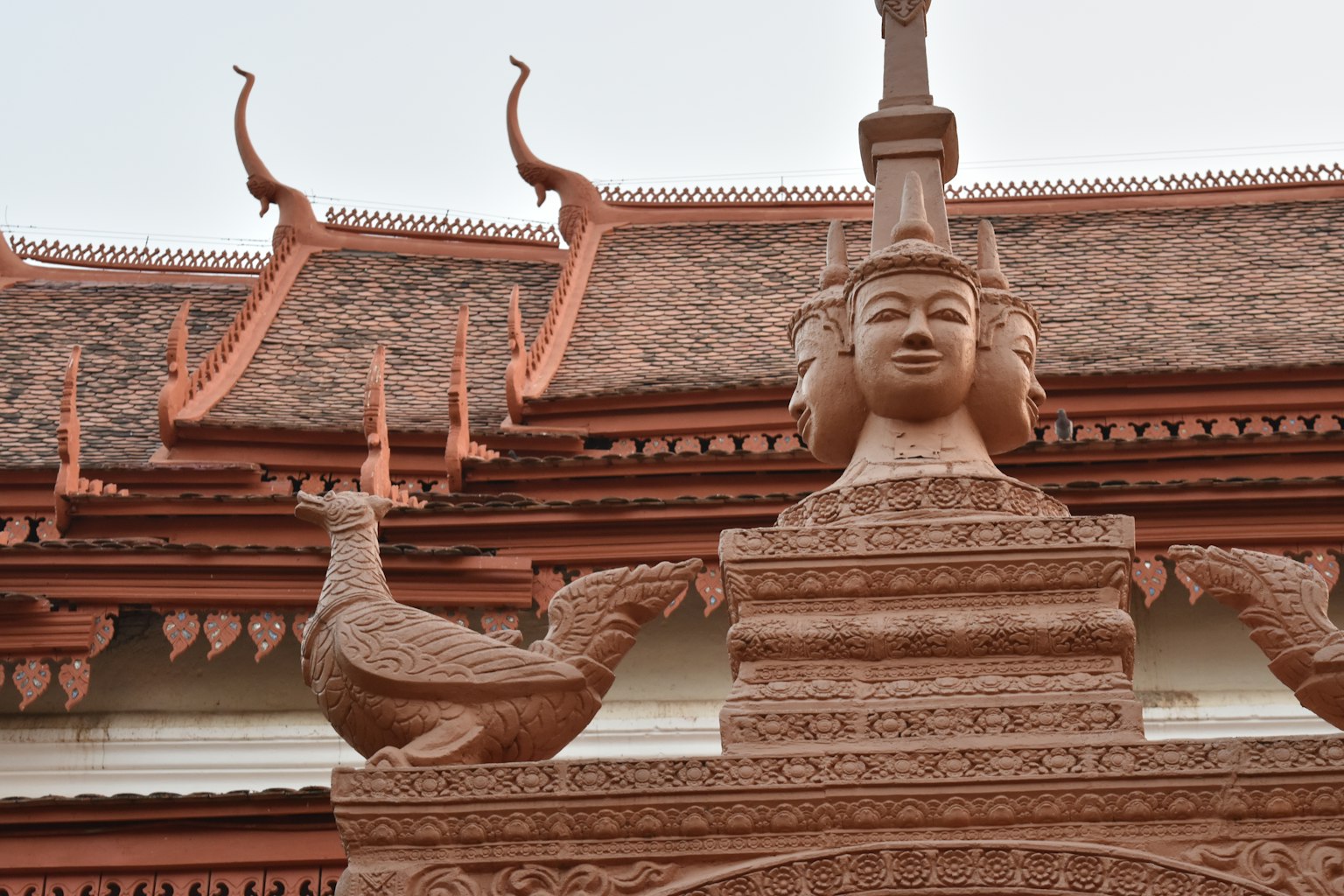 รูปปั้นประดับใบหน้าของผู้หญิงและนกยูงบนวัดสีน้ำตาลแดง