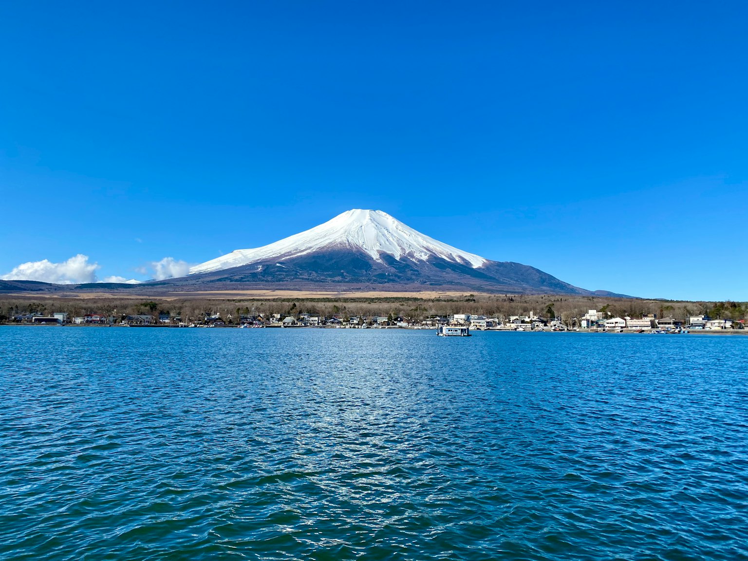 Il maestoso Monte Fuji si erge contro un cielo blu chiaro sopra un lago tranquillo
