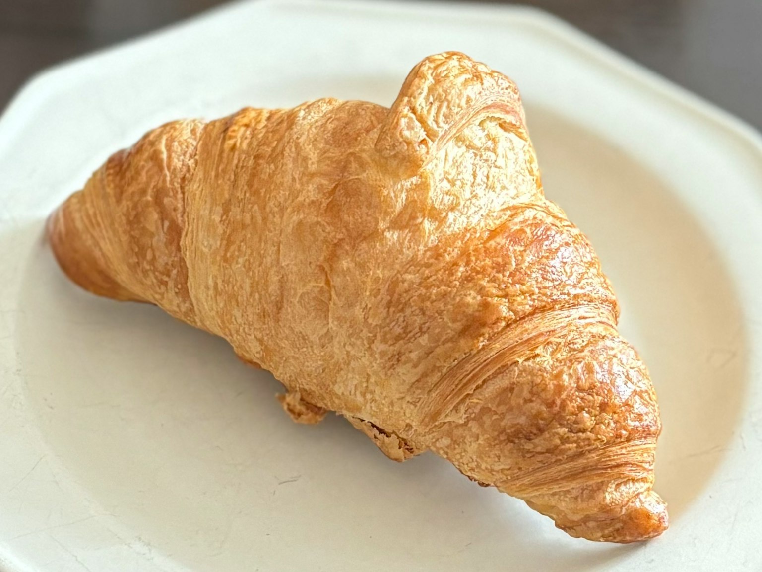 Goldbrauner, blätteriger Croissant auf einem weißen Teller