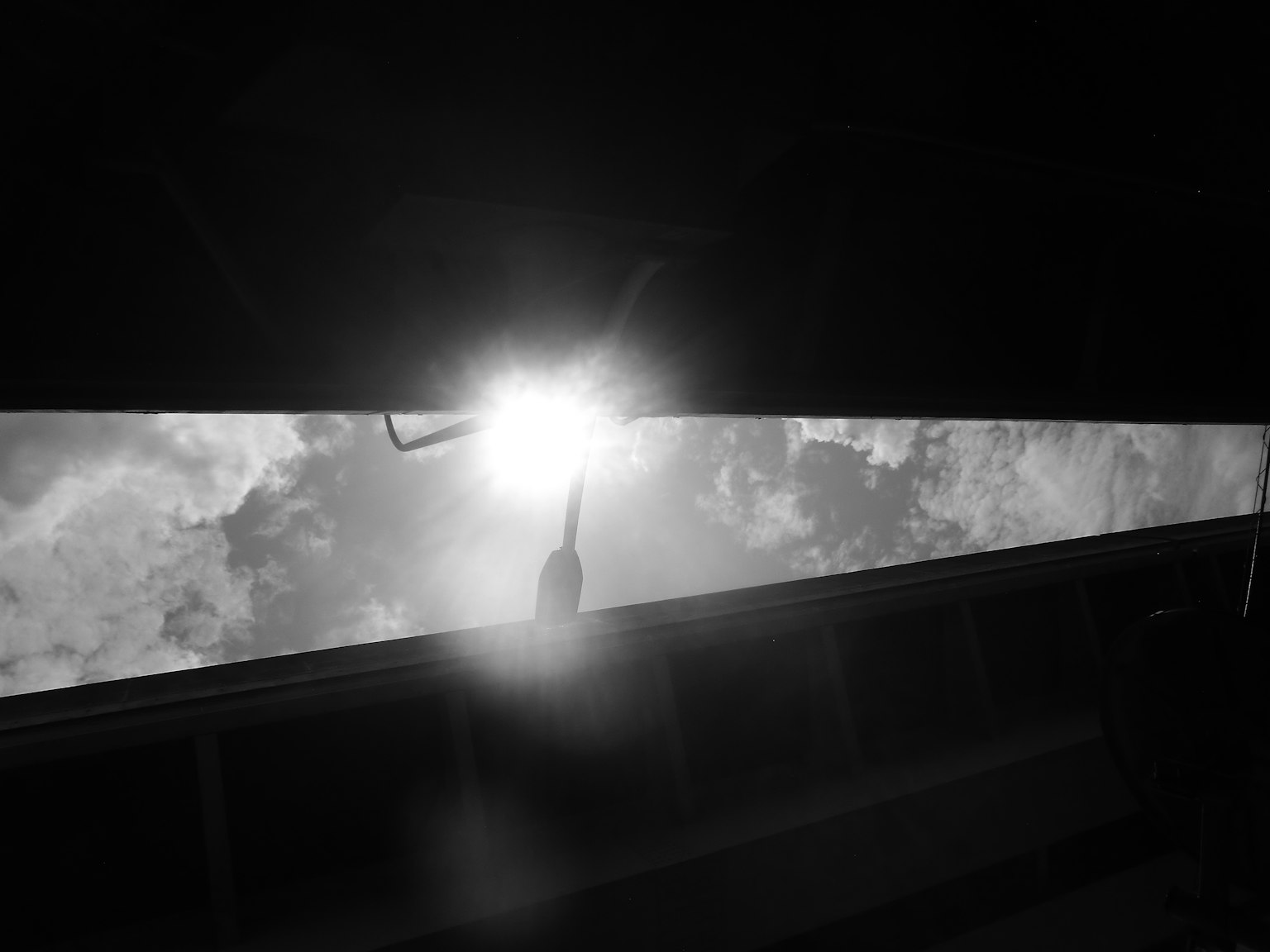 Imagen en blanco y negro que muestra luz que entra por una abertura con nubes al fondo