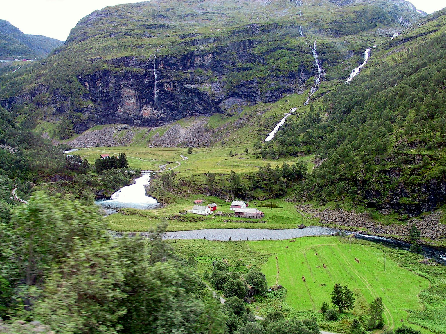 Paisaje escénico con montañas y campos verdes un río que fluye y pequeñas granjas dispersas