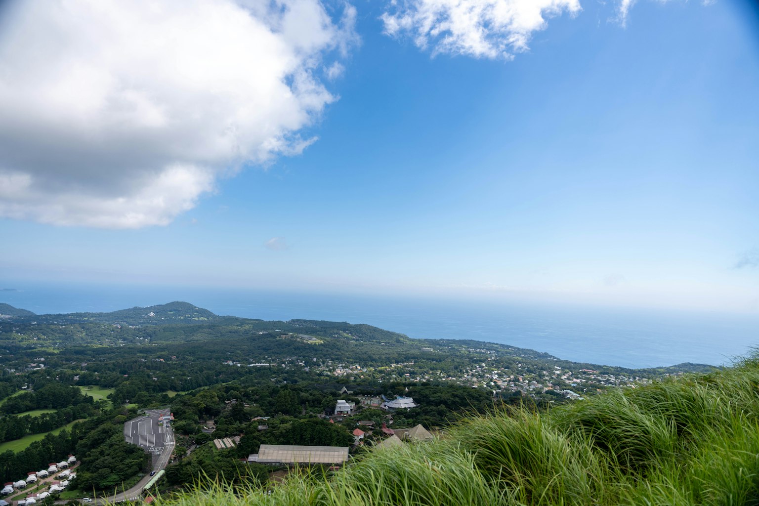 Pemandangan panorama perbukitan hijau dan lautan di bawah langit biru dengan awan