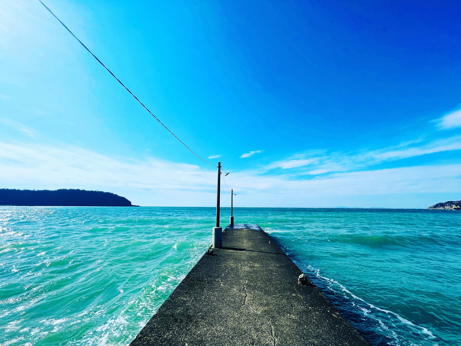 Pemandangan dermaga yang membentang ke laut turquoise di bawah langit biru yang cerah