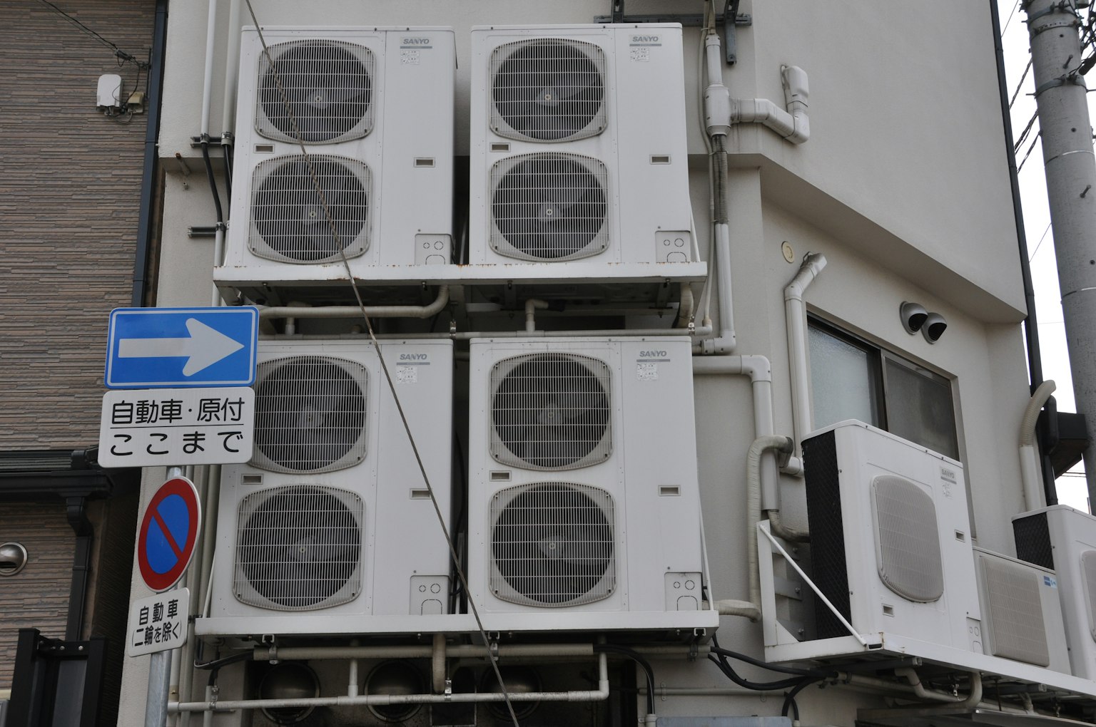 四個空調單元安裝在建築牆上，旁邊有交通標誌