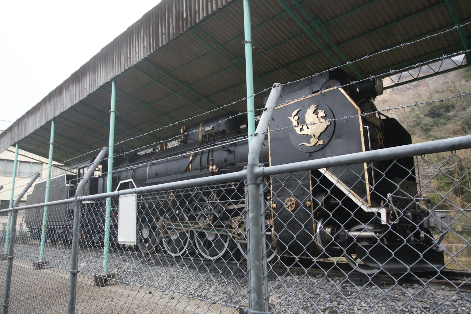一輛黑色蒸汽機車在屋頂下展示，周圍有圍欄