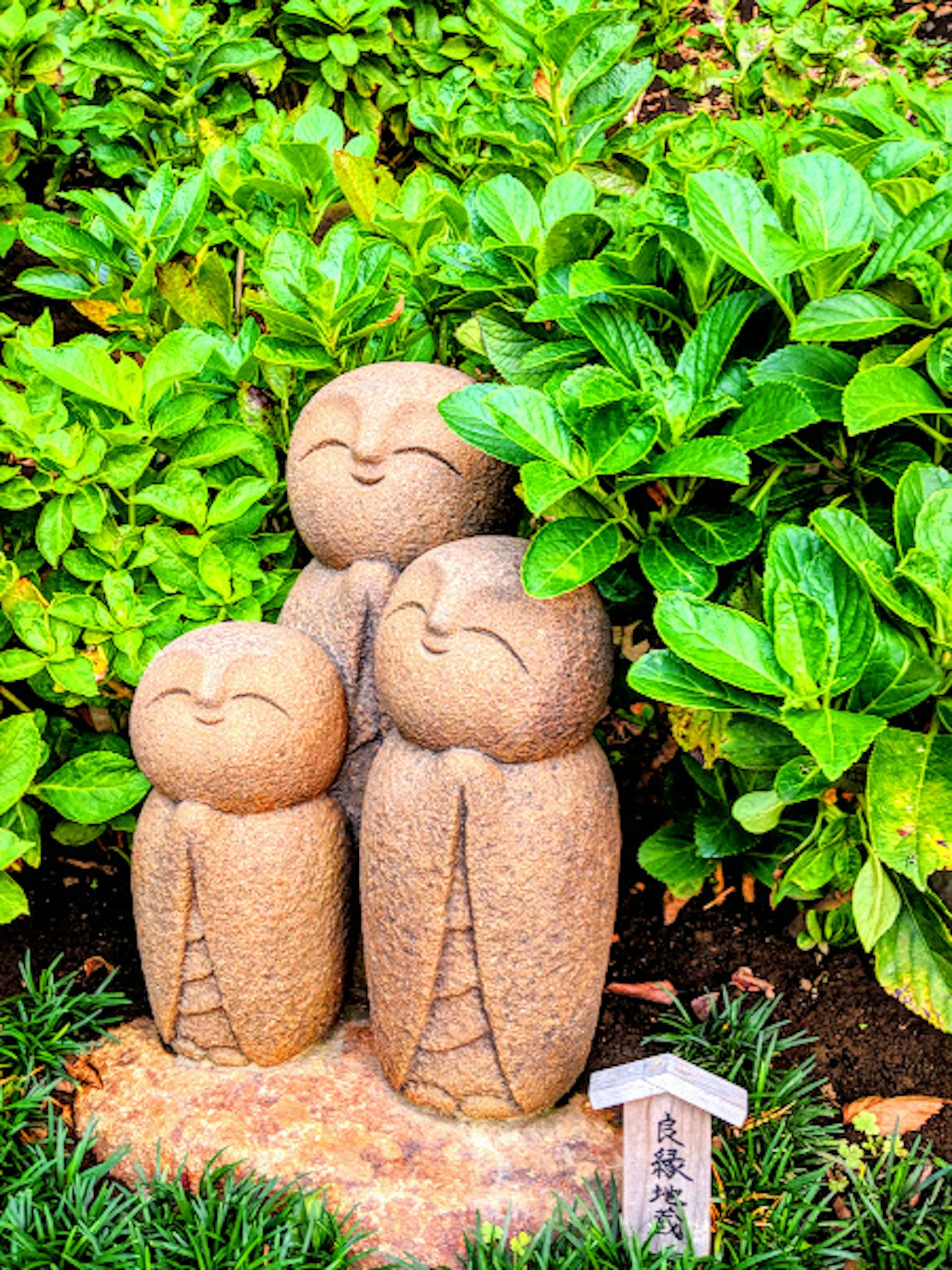 Tres adorables esculturas de piedra en un jardín rodeadas de plantas verdes exuberantes con caras sonrientes