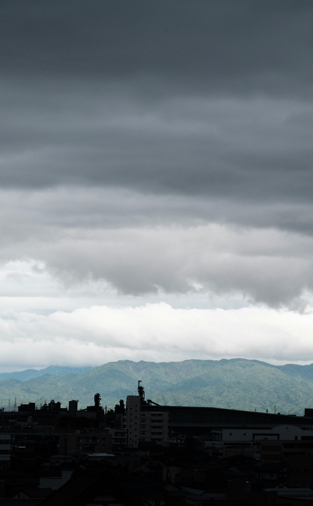 雲が広がる空と山並みを見下ろす街の風景