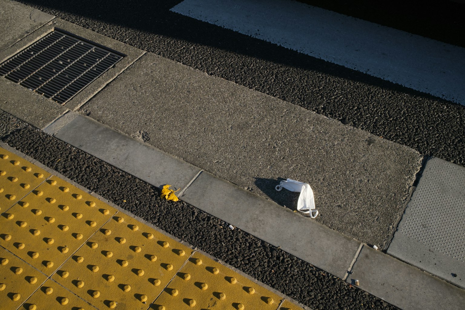 Image of a train station platform showing textured tiles and pavement yellow tactile paving and a white object in focus