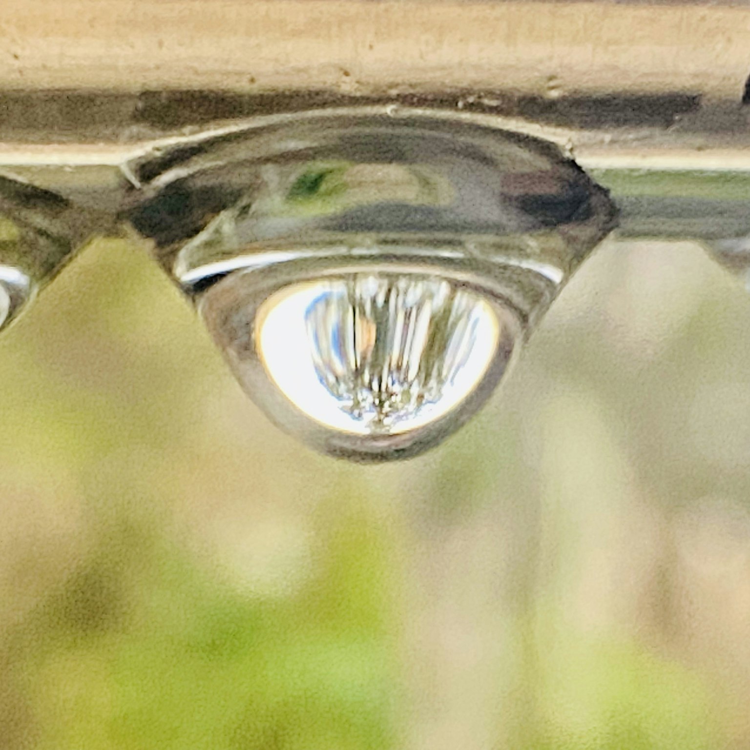 Ein Wassertropfen hängt an einer Metalloberfläche mit Reflexionen