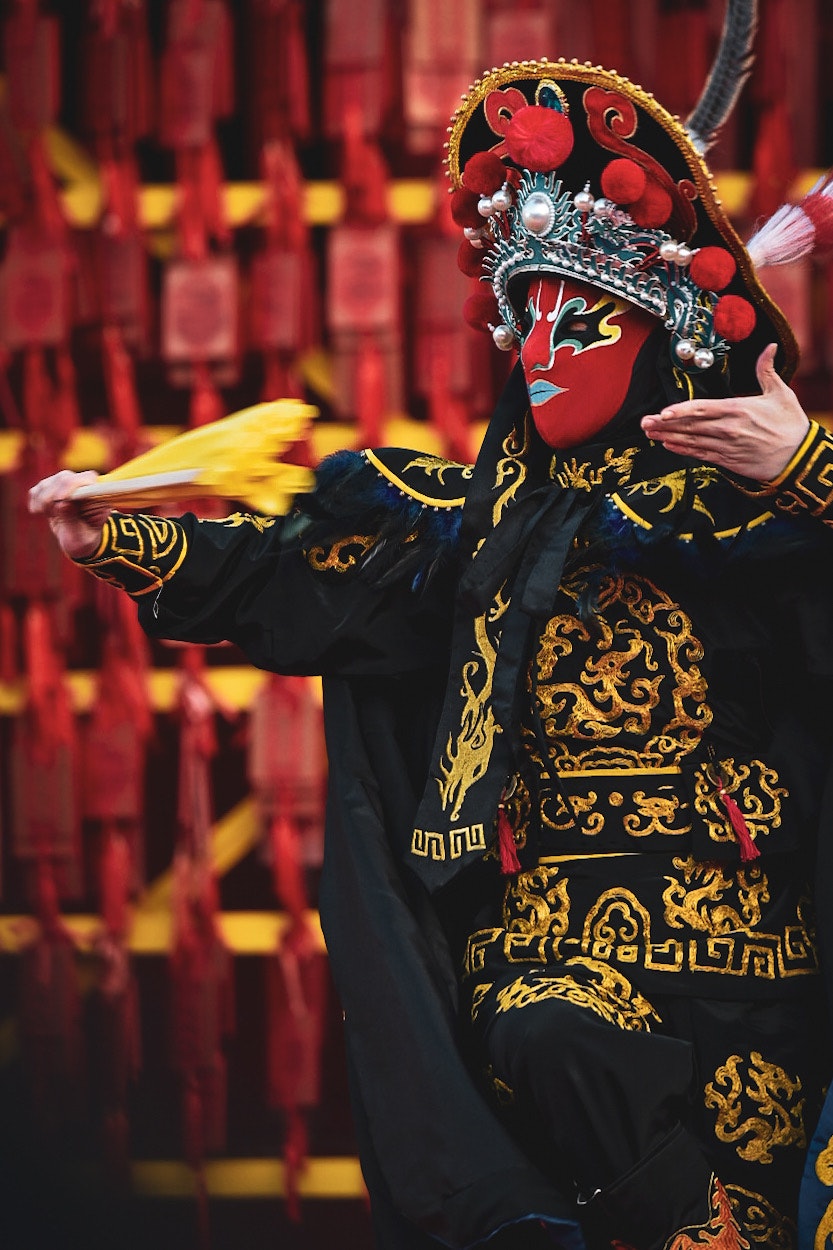 伝統的な中国のパフォーマンスで衣装を着た人物が舞台で演じている様子 赤い背景に装飾が施されている