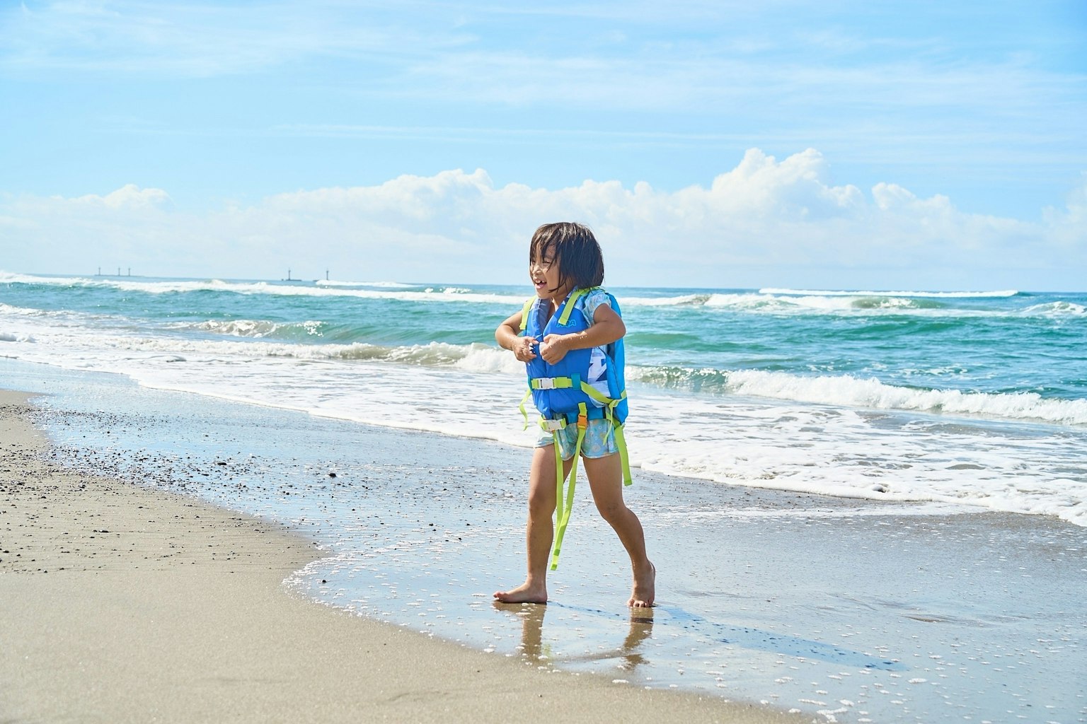 Bambino che gioca sulla spiaggia con cielo blu e onde
