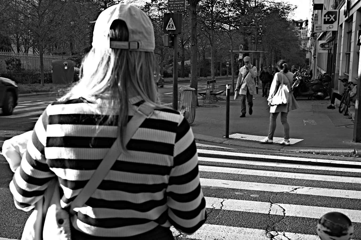 Seorang wanita berpakaian garis-garis mengamati wanita lain berpakaian putih di zebra cross