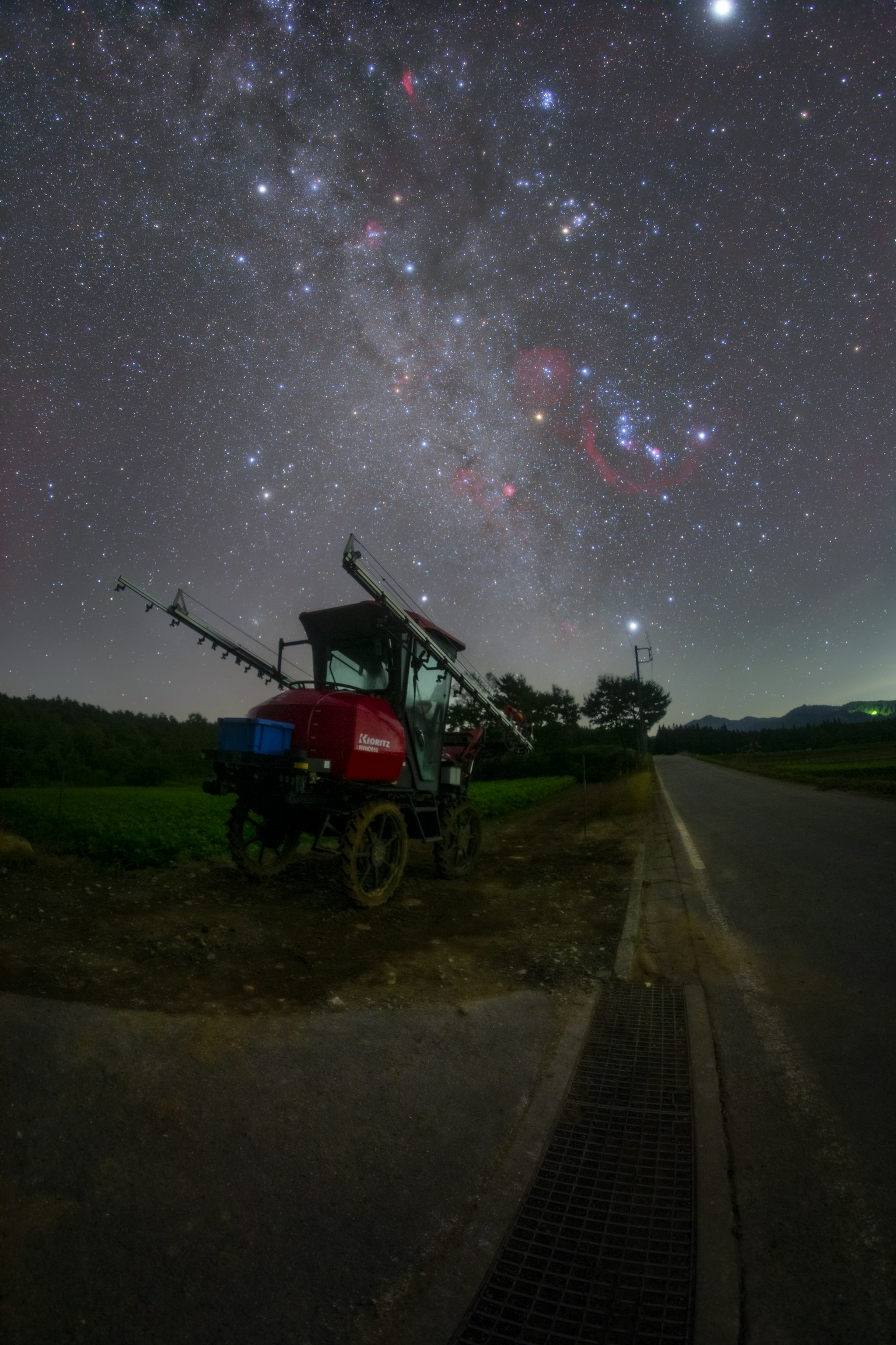 Red tractor beside a rural road under a starry sky