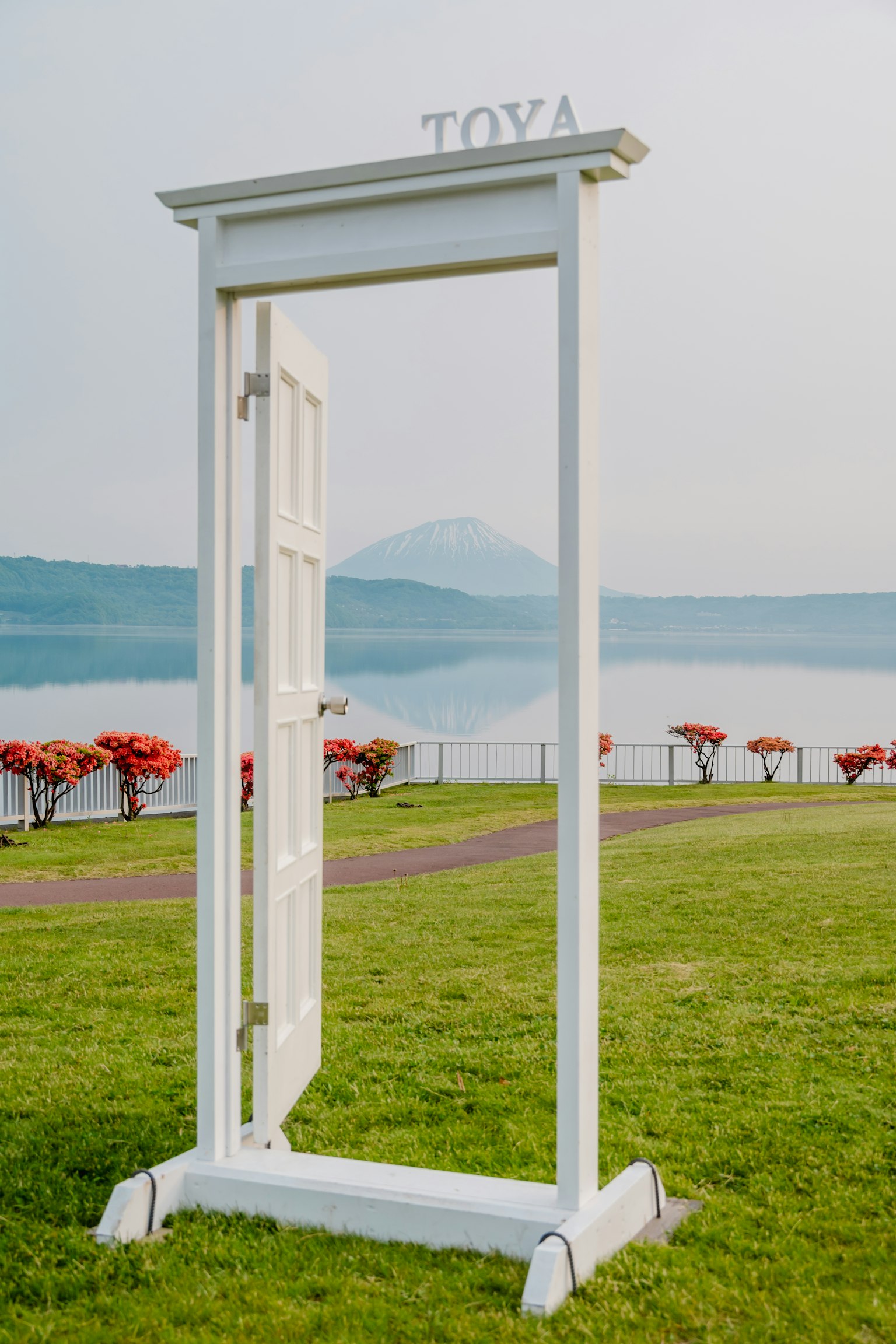 Una porta bianca che si erge vicino a un lago con il monte Fuji sullo sfondo