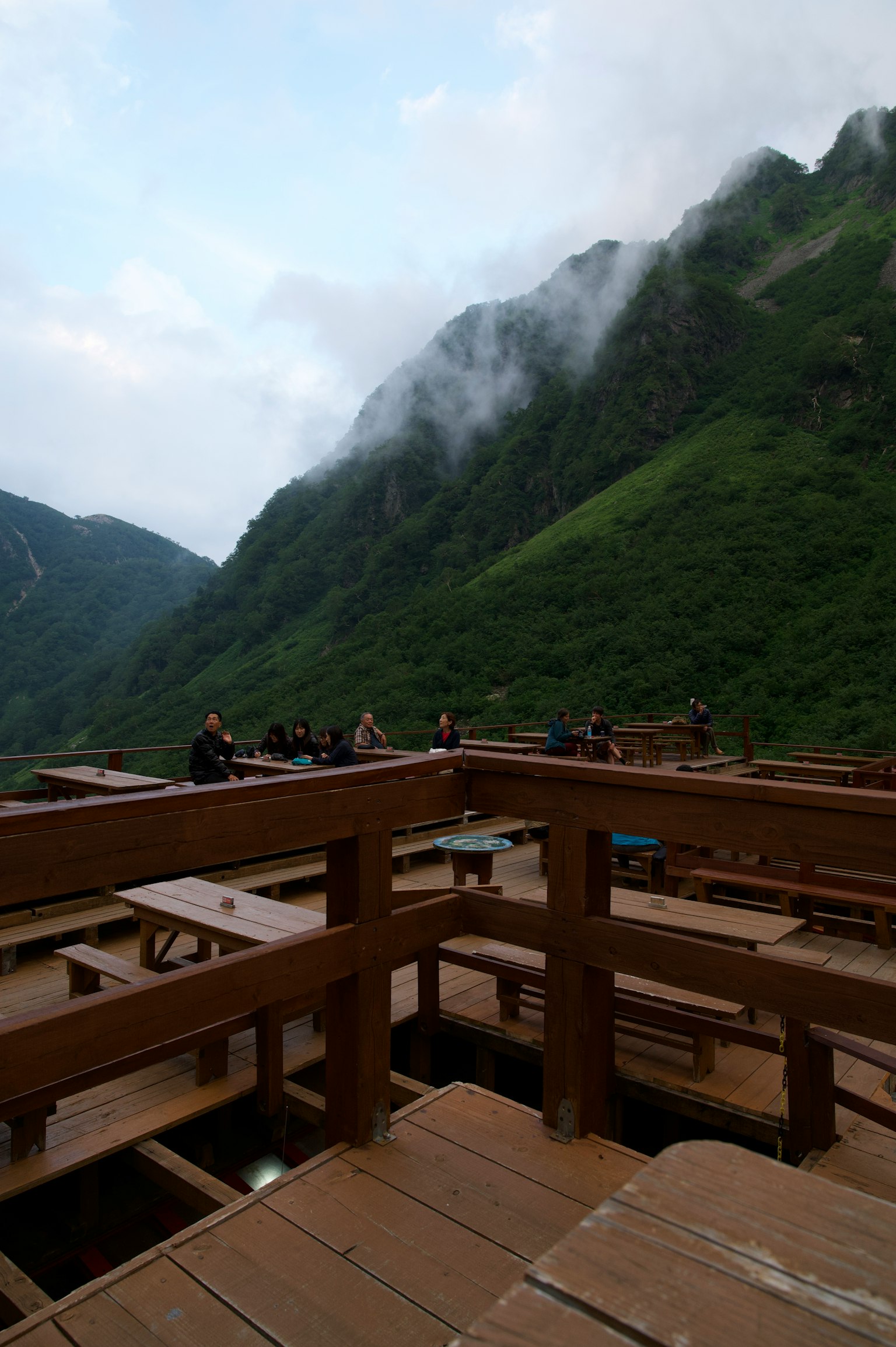 Wooden terrace with people gathering surrounded by mountains and mist