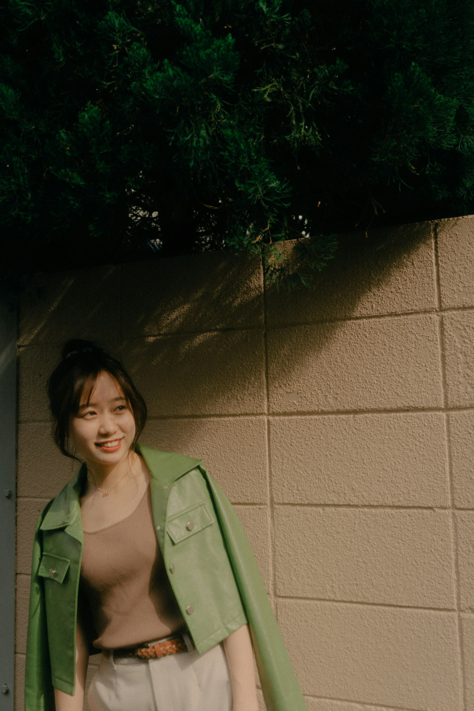 一位穿著綠色夾克的女性在牆前微笑