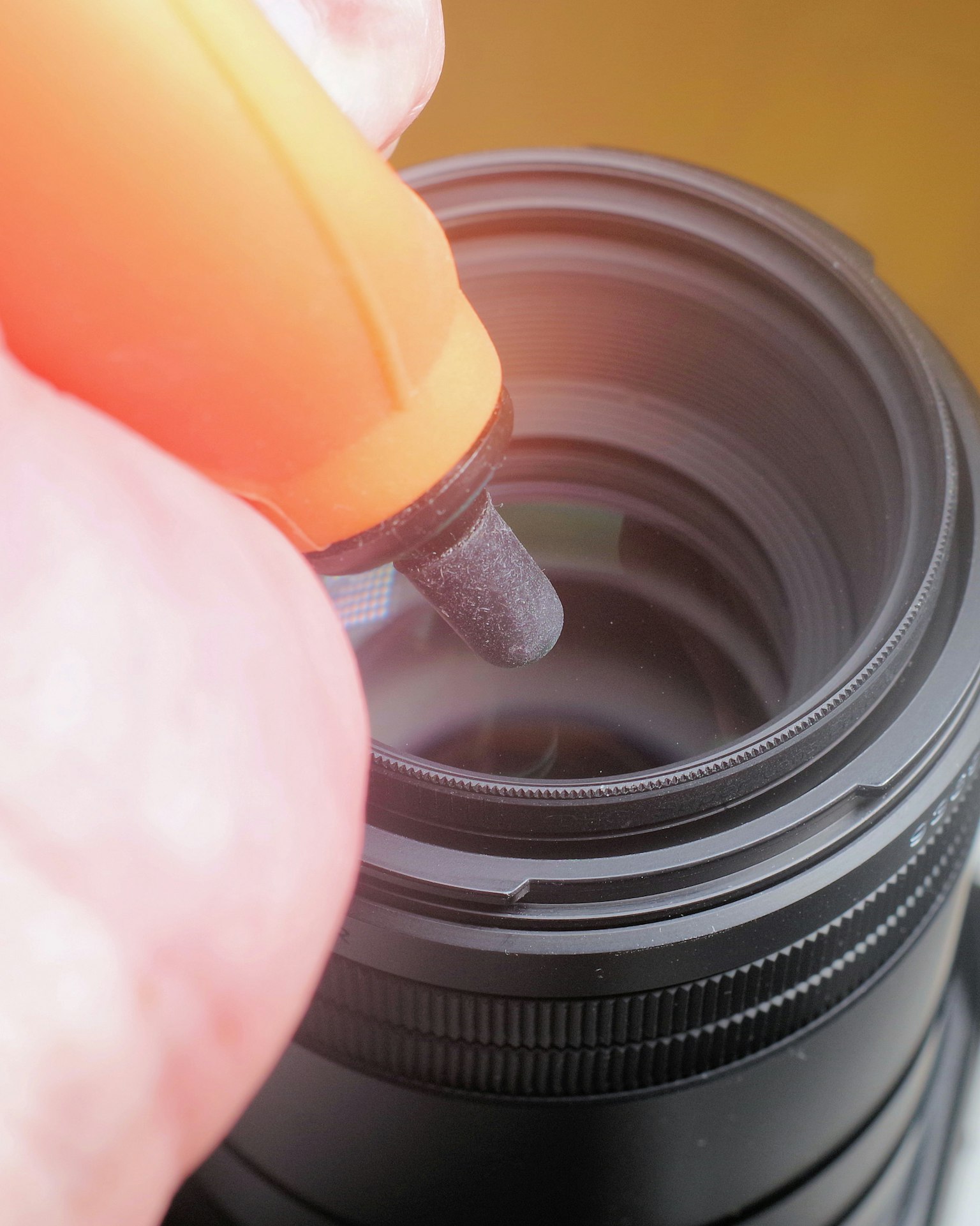 Hand, die einen orangefarbenen Stift verwendet, um das Innere eines Kameraobjektivs zu reinigen