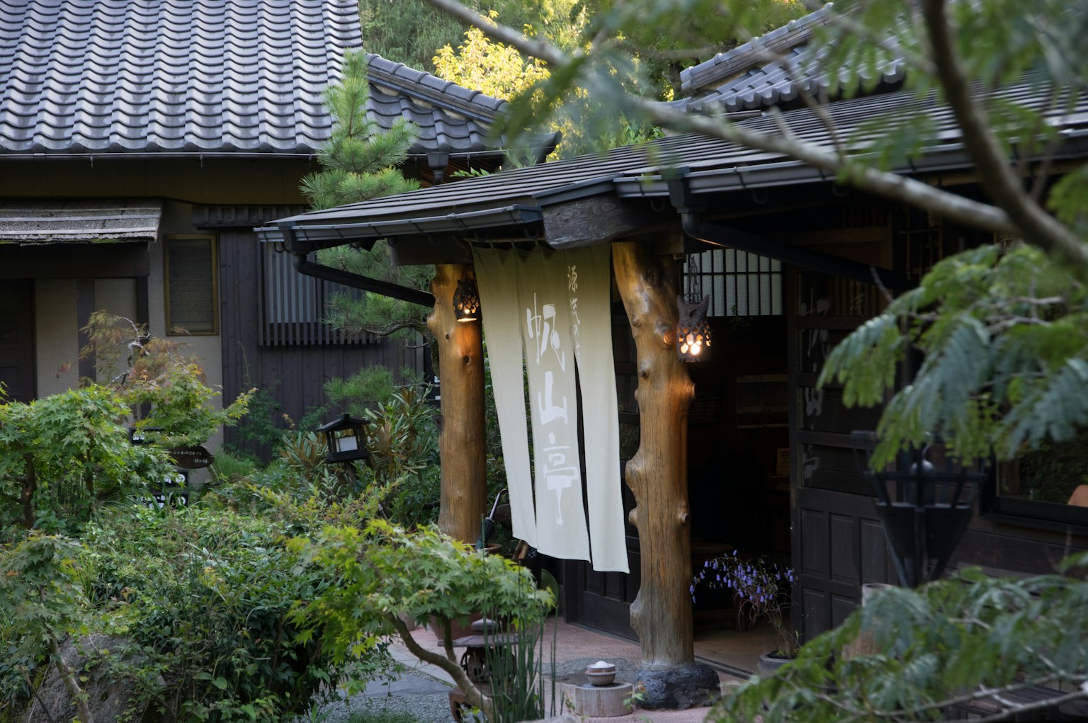 Entrance of a traditional Japanese house with a white noren and lush garden