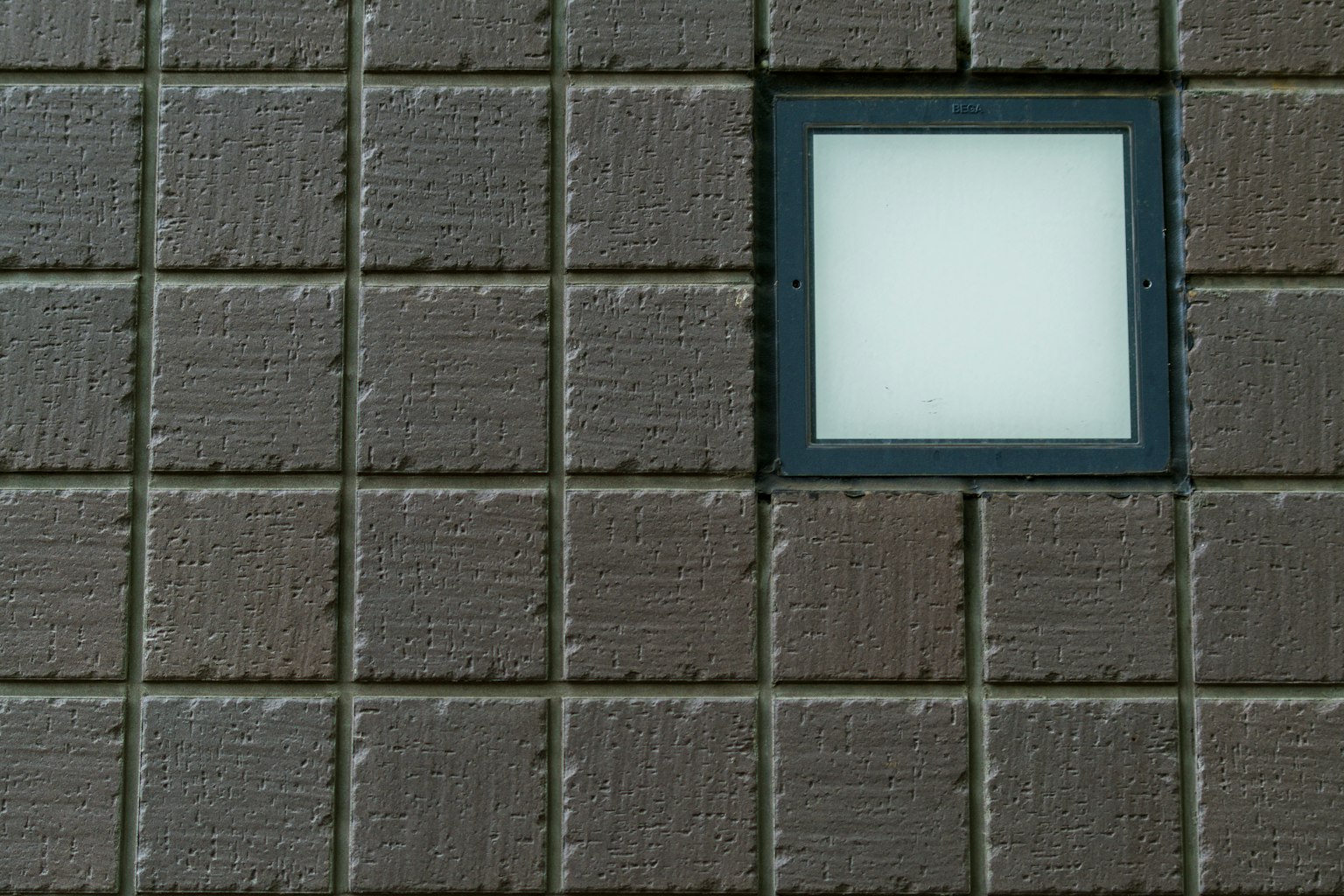 Apparecchio luminoso bianco quadrato su muro brunito texturizzato