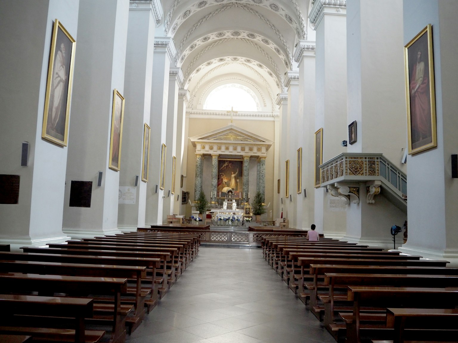 Innenraum einer geräumigen Kirche mit langen Bänken und einer hohen Decke mit lebhaften Gemälden an den Wänden