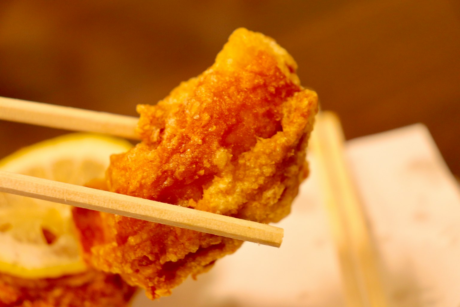 Un trozo de pollo frito sostenido con palillos junto a una rodaja de limón